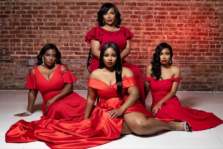 three women in red dresses sitting on the floor next to a brick wall, posing for a photo