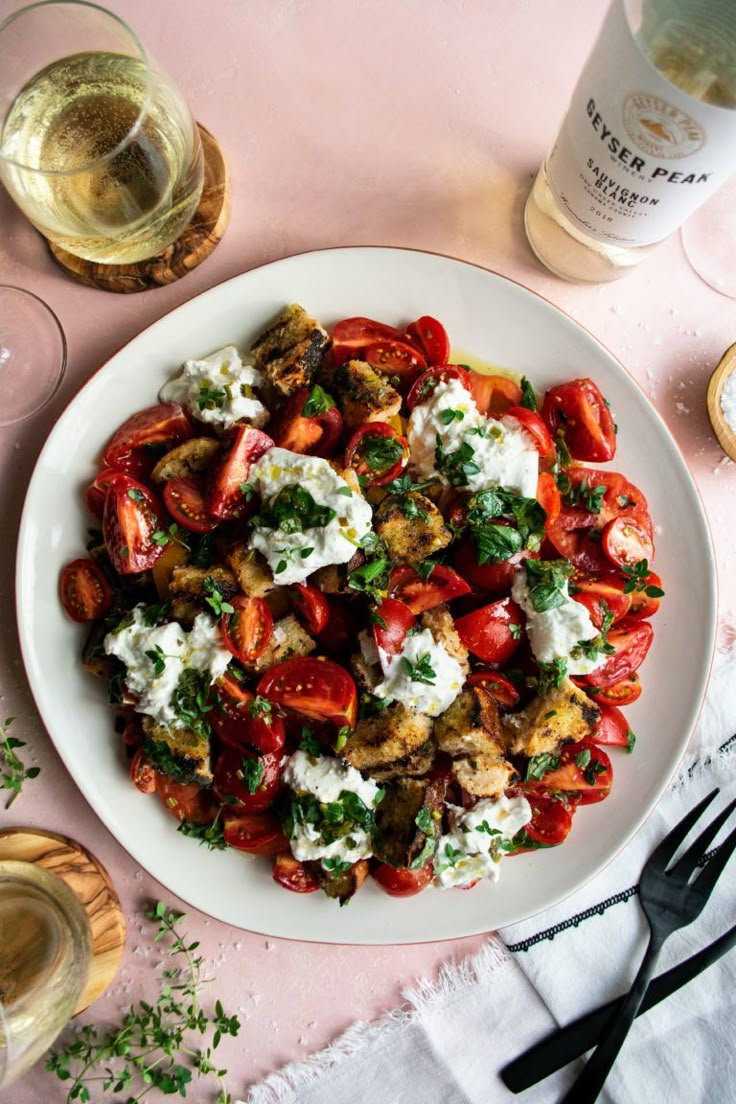 a white plate topped with lots of food next to wine glasses and utensils