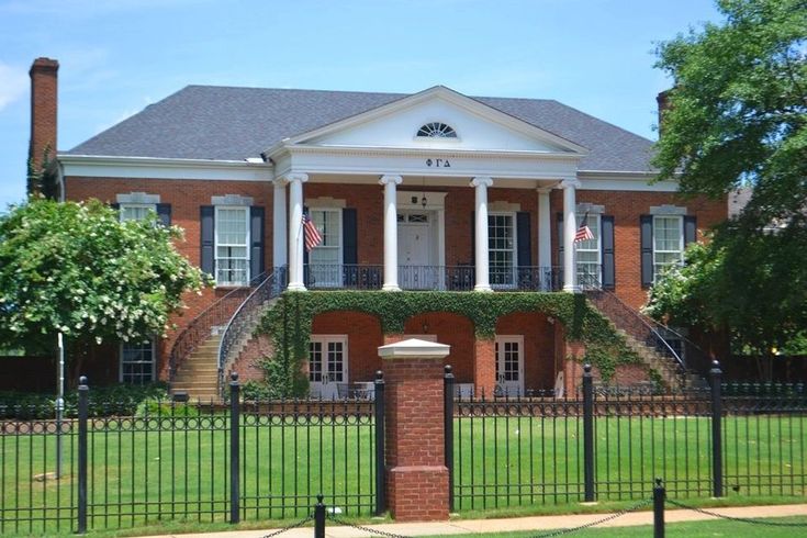 a large red brick house with columns and pillars on the front porch, surrounded by lush green grass