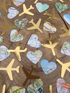 many heart shaped paper cutouts are arranged on a wooden table with an airplane and map in the middle