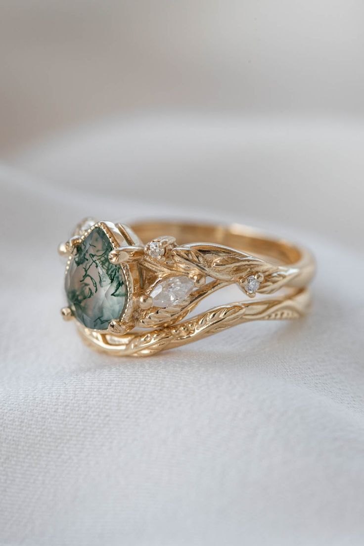 a gold ring with green and white stones on it's sides, sitting on a white cloth