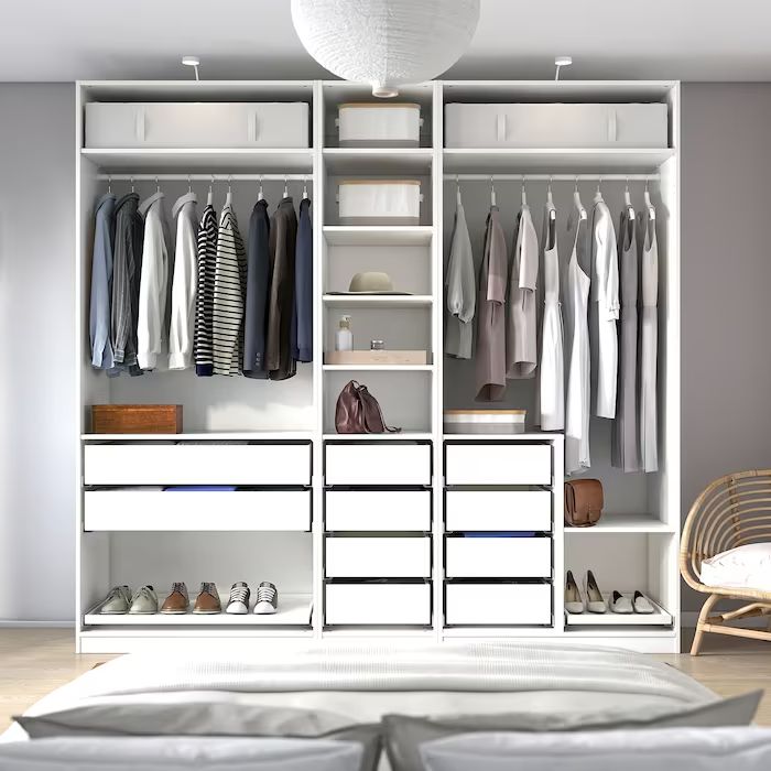 an open closet with clothes and shoes on shelves next to a bed in a bedroom