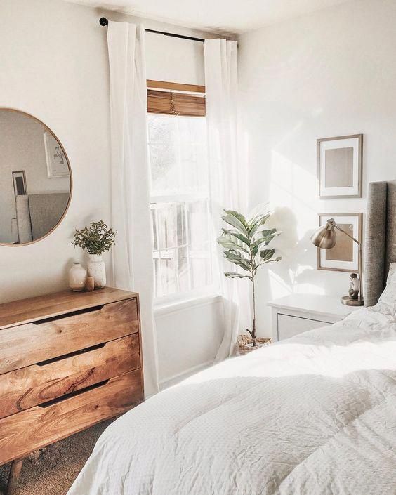 a bedroom with white bedding and wooden dresser in front of a large mirror on the wall