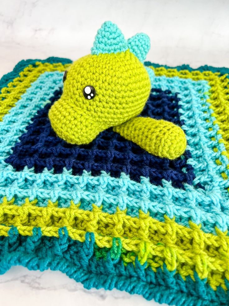 a crocheted stuffed animal laying on top of a blue and green blanket with squares