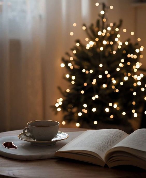 an open book on a table with a cup and saucer in front of a christmas tree