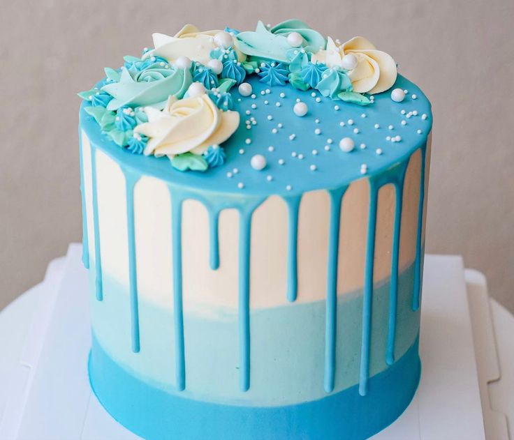 a cake with blue icing and white flowers on top is sitting on a table