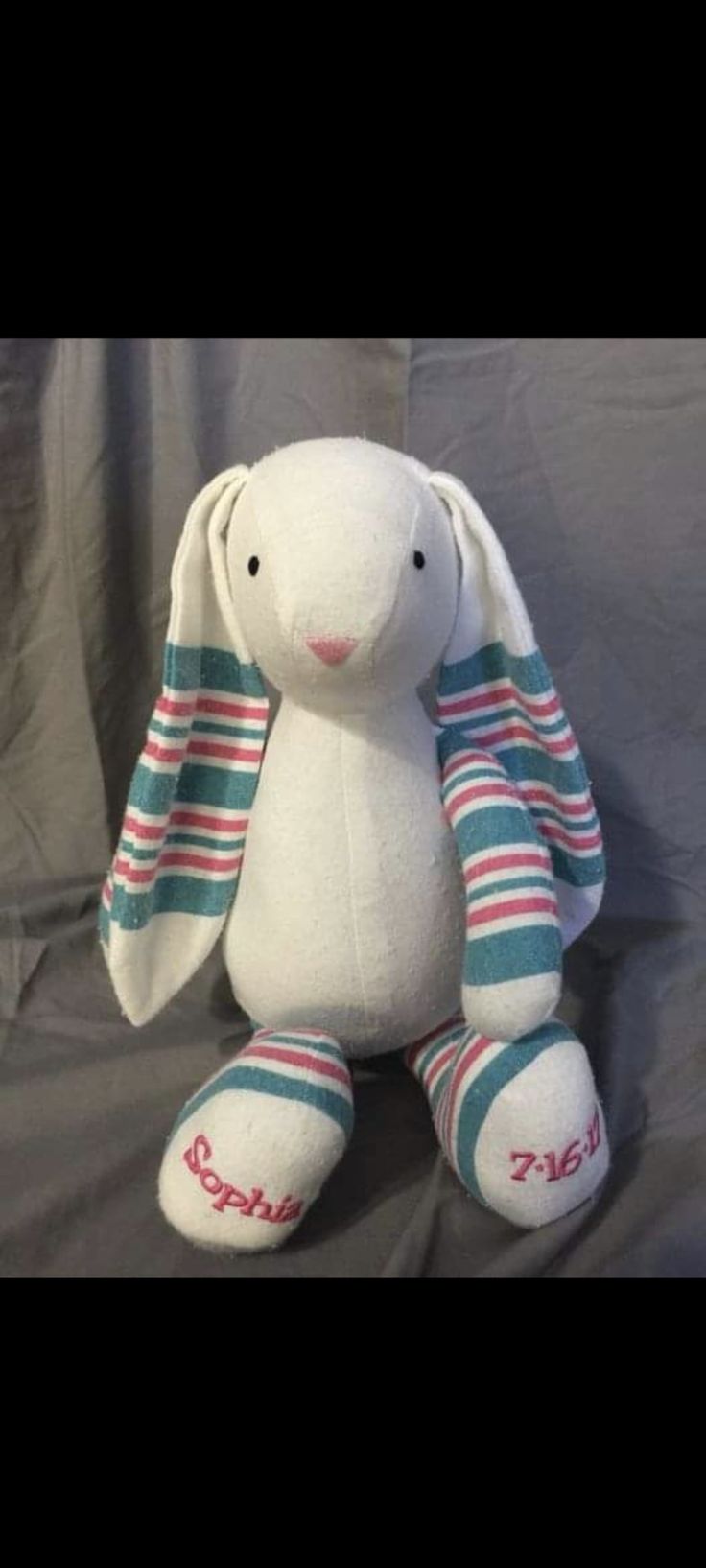 a white stuffed rabbit with blue and red stripes on it's ears, sitting in front of a gray background