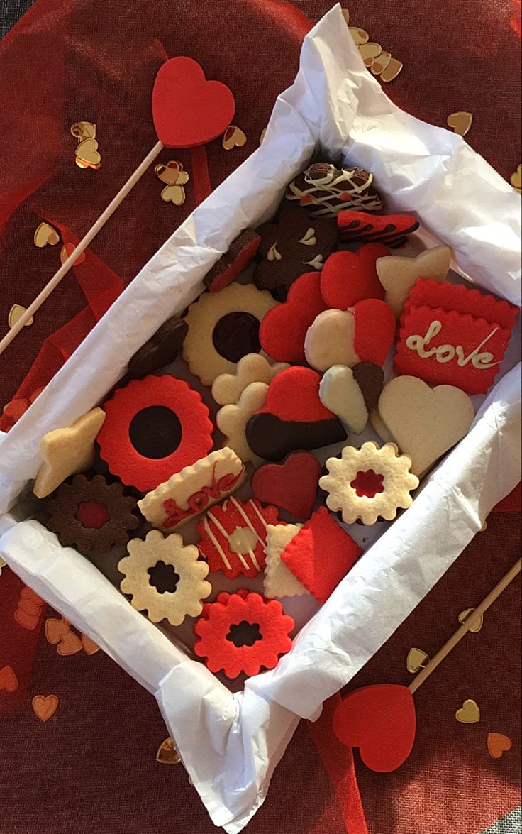 a box filled with lots of decorated cookies on top of a red table cloth covered in hearts