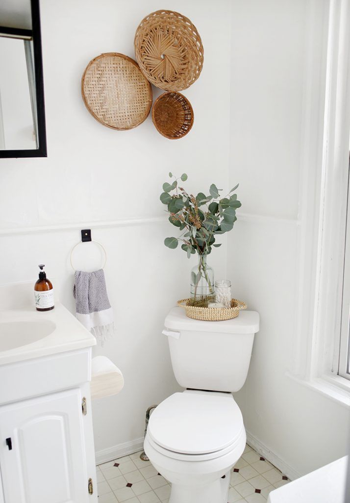 a white toilet sitting in a bathroom next to a sink and a window with wicker baskets on the wall above it