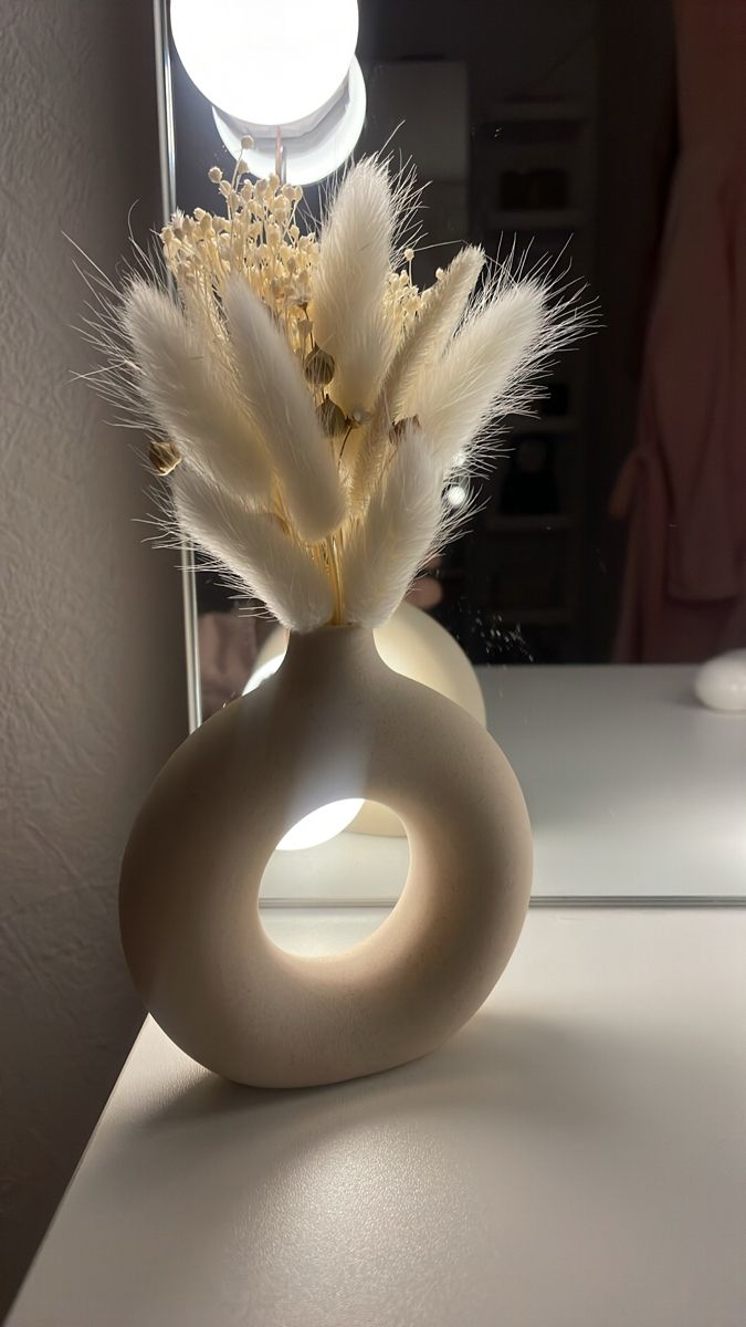 a white vase filled with feathers on top of a table next to a light bulb