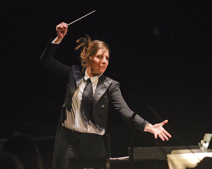 a woman in a suit and tie holding a conductor's baton with both hands