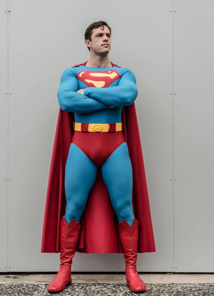 a man dressed as superman standing in front of a wall with his hands on his hips