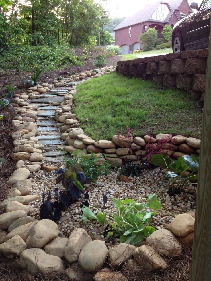 there is a garden with rocks and plants in the ground next to a car parked on the side of the road