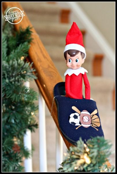 an elf is sitting on top of a christmas tree with a blue bag in front of him