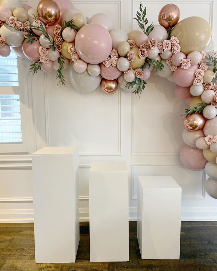 balloons and flowers are arranged on the wall in front of two white pedestals, one with