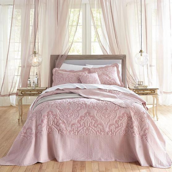 a bed with pink comforter and pillows in a room next to a window,