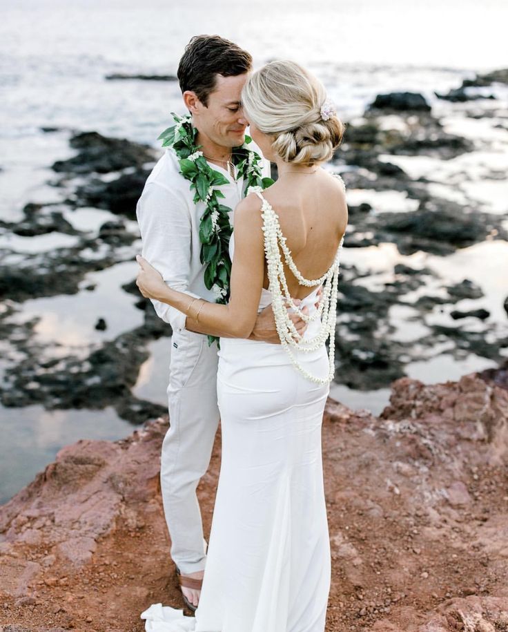 a man and woman standing next to each other near the ocean with their arms around each other