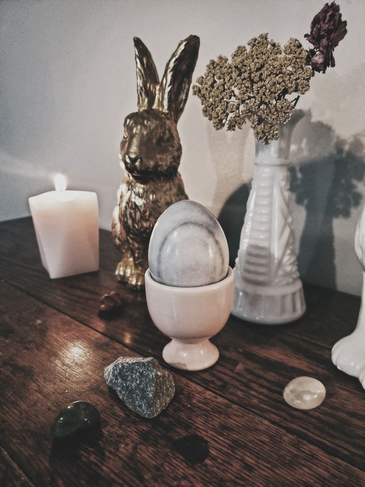 a wooden table topped with white vases filled with flowers and rocks next to candles