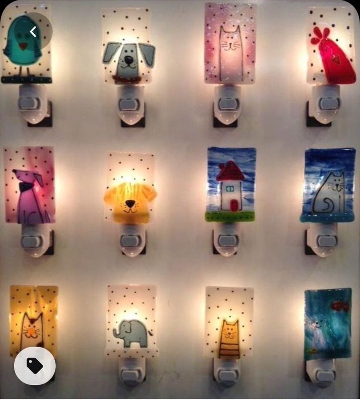 some lights are hanging on the wall with animals and houses painted on them in different colors