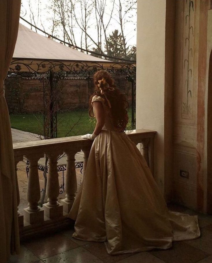 a woman in a long dress is standing on a balcony looking out at the yard