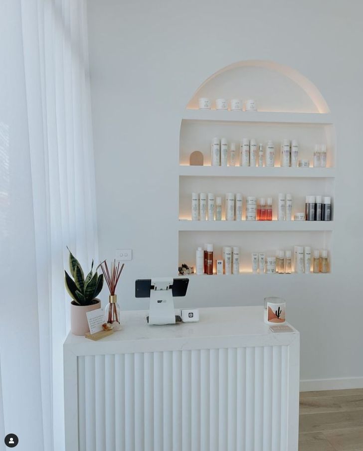 a white counter topped with lots of bottles next to a wall mounted shelf filled with candles