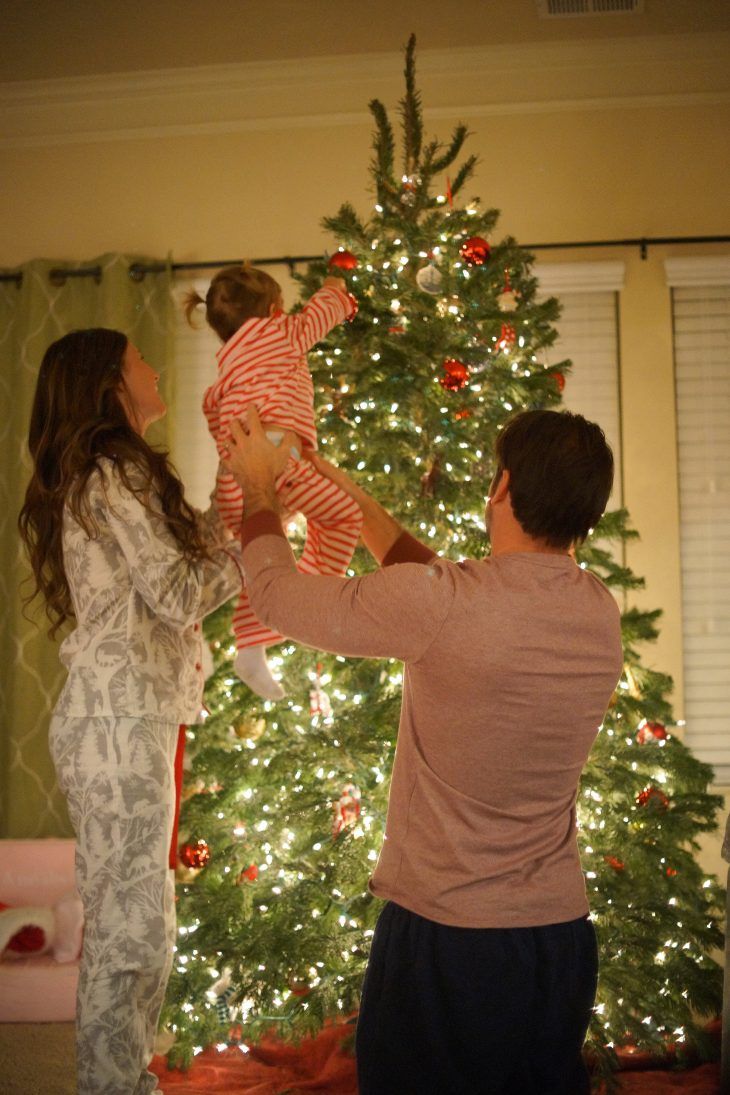 a man and woman standing in front of a christmas tree with a child on his lap