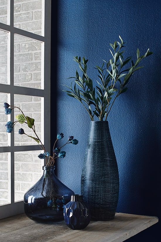 two vases with flowers are sitting on a window sill in front of a blue wall