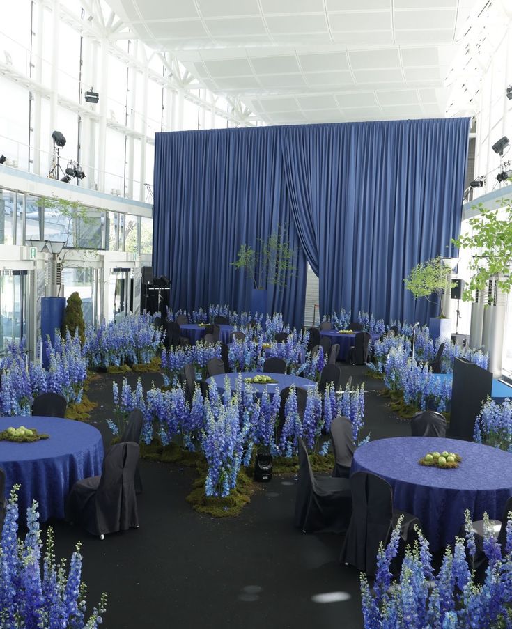 a room filled with tables covered in blue cloths and purple flower centerpieces