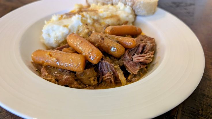 a white plate topped with meat, potatoes and gravy on top of a wooden table