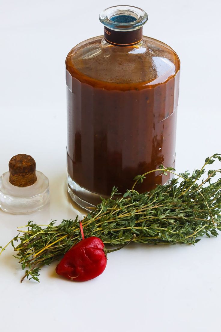 a bottle of ketchup next to a sprig of rosemary and a pepper