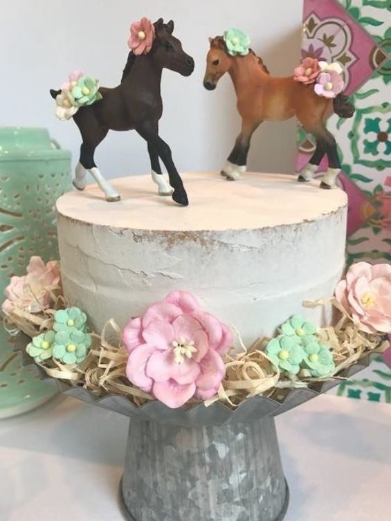 there is a cake decorated with two horses on top and flowers in the bottom tier