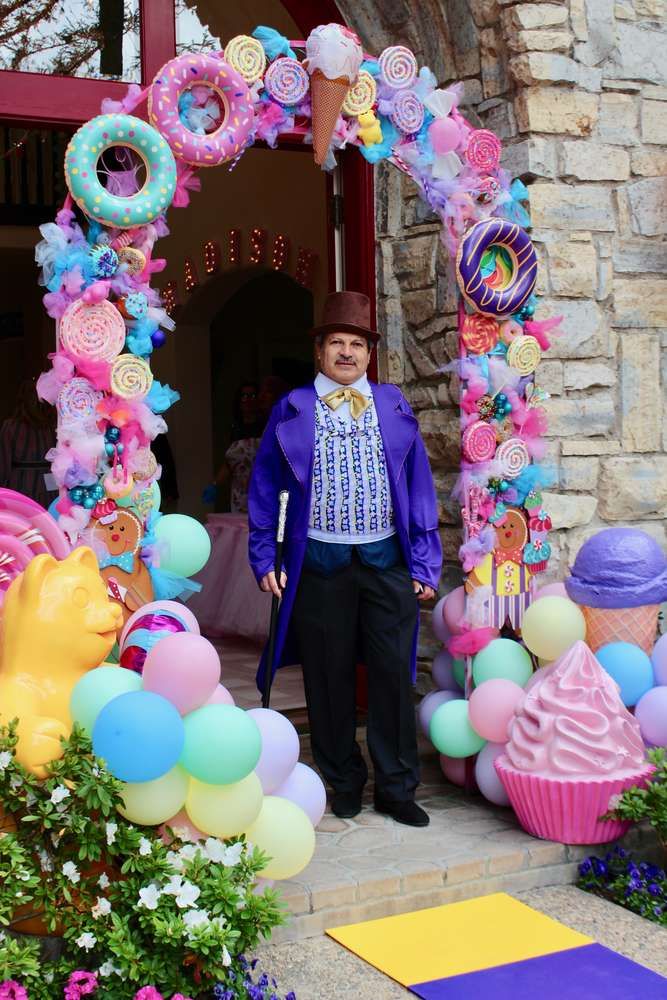 a man standing in front of a decorated arch with balloons and cupcakes on it