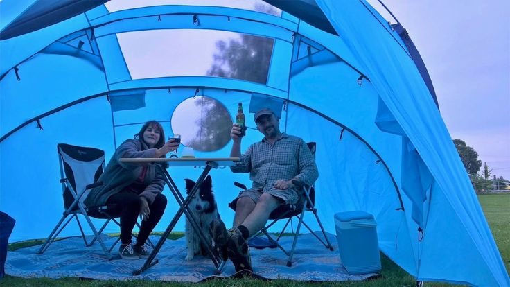 two people sitting at a table in a tent with a dog on the ground next to them