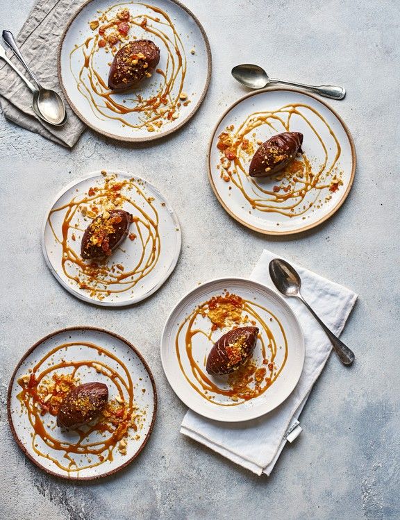 four white plates topped with desserts on top of a gray tablecloth next to spoons and utensils