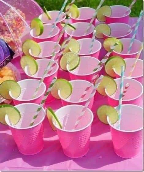 pink cups with limes, strawberries and lemon slices on them sitting on a table