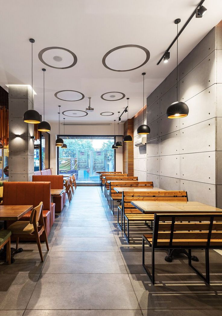 an empty restaurant with wooden tables and brown chairs on either side of the table are hanging lights