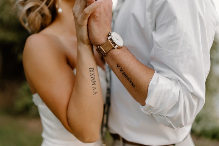 a man and woman holding each other's hands with tattoos on their arms while standing next to each other