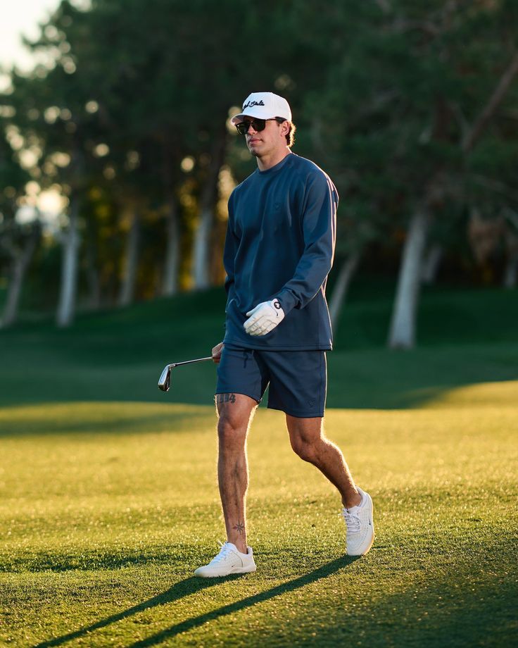 a man walking across a lush green field holding a golf racquet in his hand