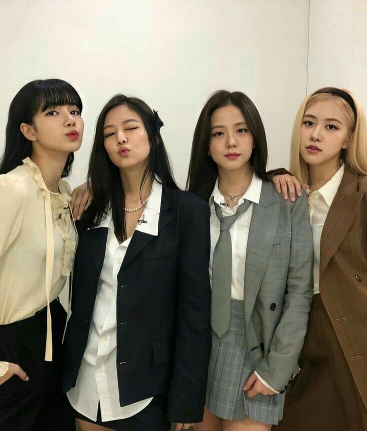 three women standing next to each other in front of a white wall wearing suits and ties