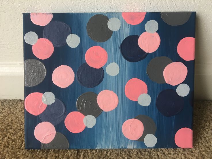 a painting with pink, black and grey circles on it sitting on the floor next to a wall