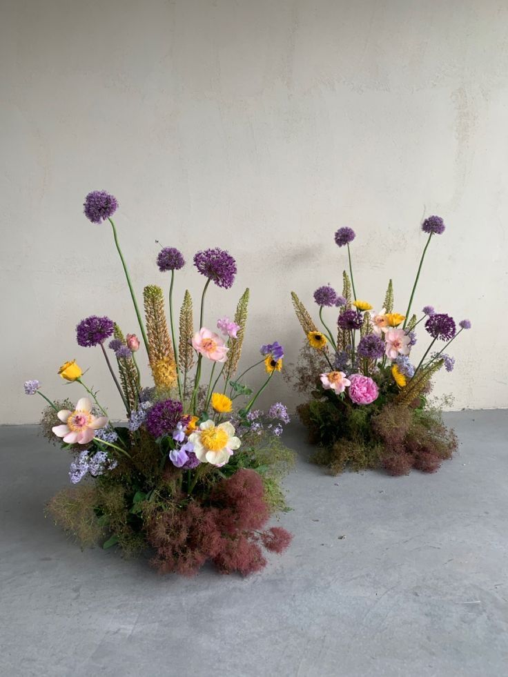 two vases filled with flowers sitting on top of a cement floor next to each other