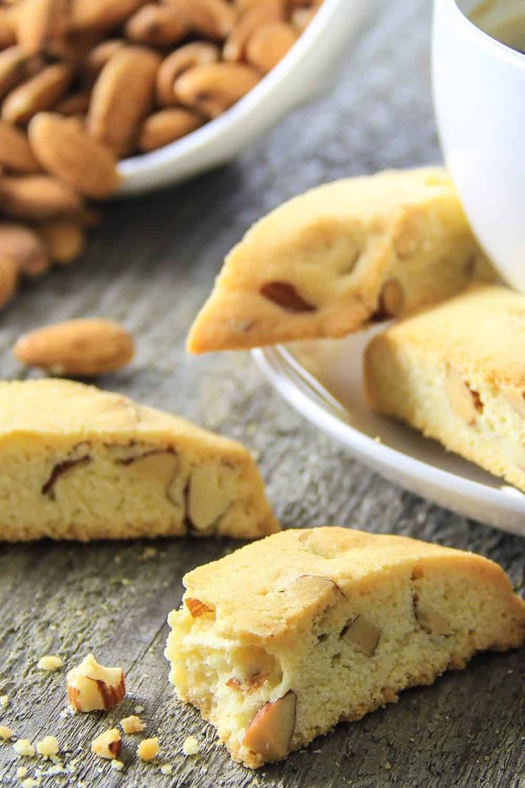 almond biscuits on a plate next to a cup of coffee and bowl of nuts