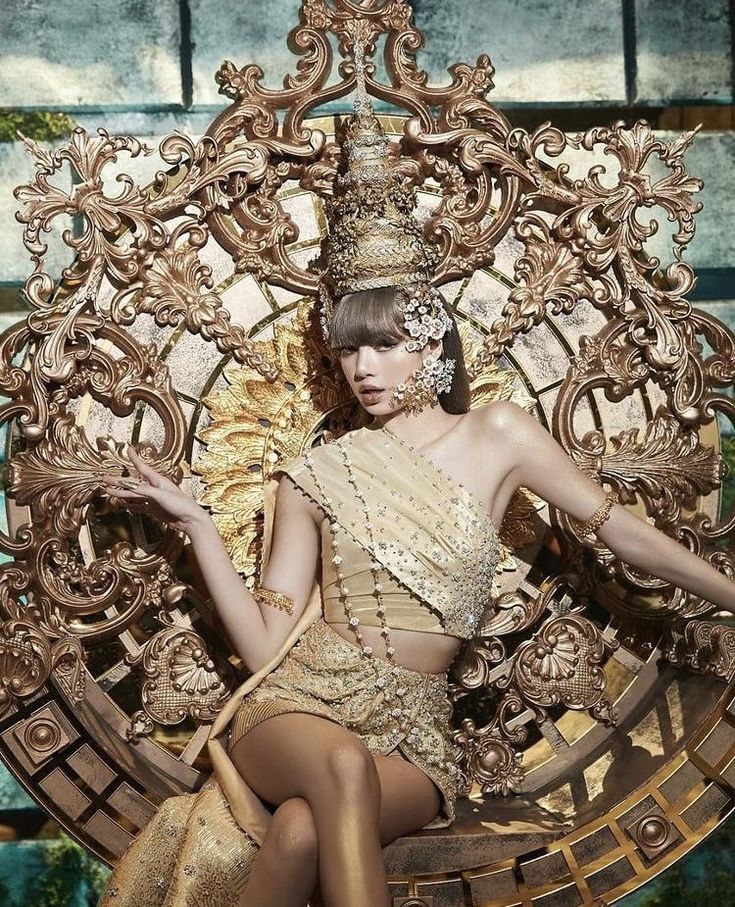 a woman sitting on top of a golden throne wearing a tiara and holding a fan