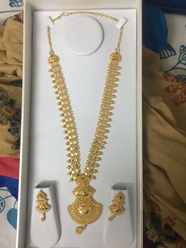 a necklace and earring set in a white box on a bed with gold jewelry