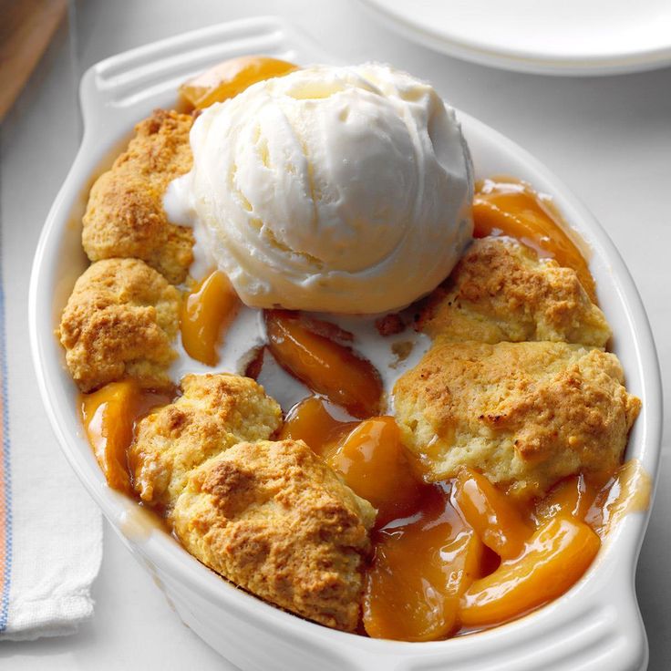 a bowl filled with ice cream and peach cobbler on top of a white table