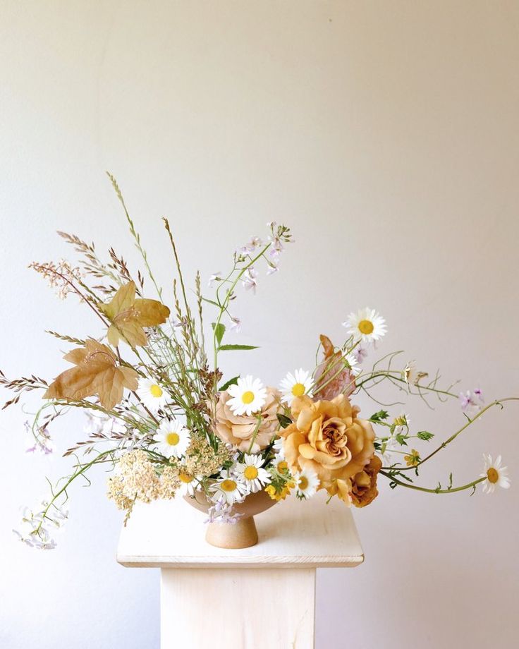 a vase filled with lots of flowers sitting on top of a white table next to a wall