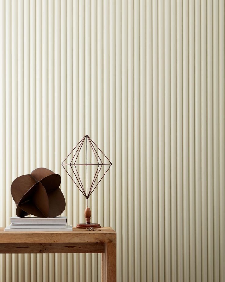 a wooden table topped with a book and a sculpture next to a wall covered in vertical blinds