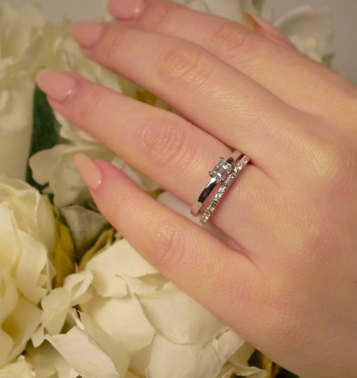 a woman's hand with a wedding ring on it and flowers in the background