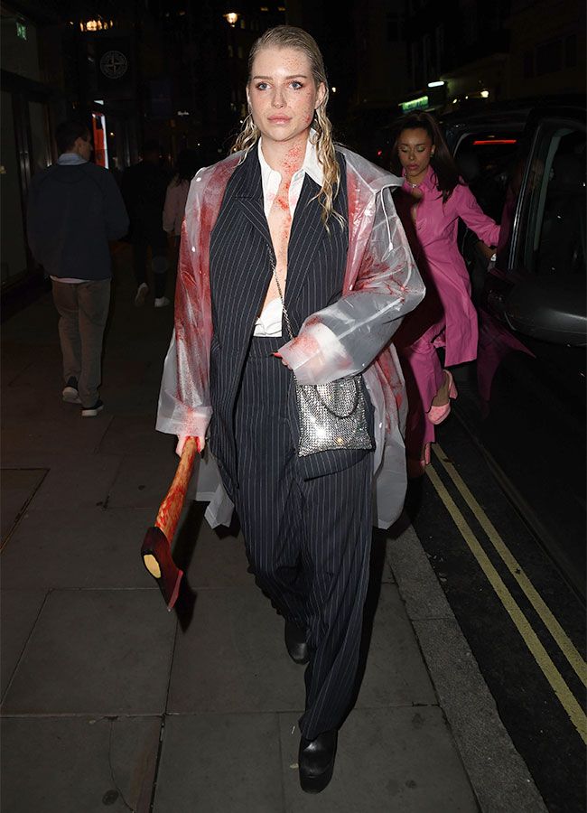 a woman walking down the street in a suit with blood all over her body and holding an umbrella