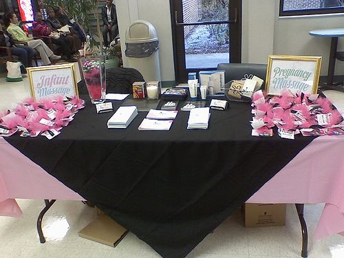 a black table with pink flowers and cards on it in front of two people sitting at tables